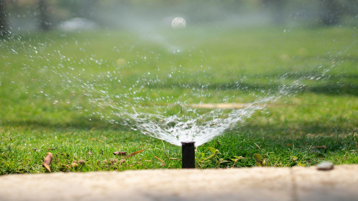 A lawn sprinkler is in operation, spraying water over green grass with a blurry background.